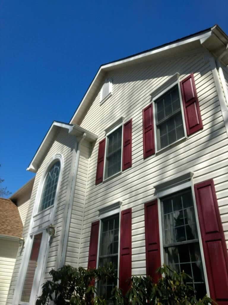 A stunning two-story house with light-colored siding and elegant maroon shutters is captured from a low angle, highlighting its architectural beauty. The home features numerous windows, including a grand arched window above the entrance that adds character to the façade. Under a clear blue sky, the property stands as an ideal example of what Maryland Pro Wash can help maintain with their expert pressure washing services. Serving Harford County MD, Baltimore County MD, Cecil County MD, Howard County MD, Carroll County MD, Anne Arundel County MD; Wilmington DE; New Castle County DE; and Delaware County PA—their professional team ensures your home looks as pristine and inviting as this one by safely removing dirt and grime to rejuvenate your siding and shutters. Trust Maryland Pro Wash to enhance your home's curb appeal throughout these regions!