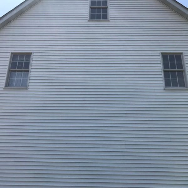 The image captures the pristine side of a white building with three windows. The horizontal lines of the siding add to its neat appearance, while sunlight creates a gentle glare near the roof's peak, highlighting the structure’s well-maintained condition. For those in search of professional cleaning services to maintain such immaculate exteriors, Maryland Pro Wash offers top-tier pressure washing solutions. Serving Harford County MD, Baltimore County MD, Cecil County MD, Howard County MD, Carroll County MD, Anne Arundel County MD as well as Wilmington DE, New Castle County DE and Delaware County PA—Maryland Pro Wash ensures your property remains just as well-kept and radiant by expertly removing dirt and grime from your outdoor surfaces.