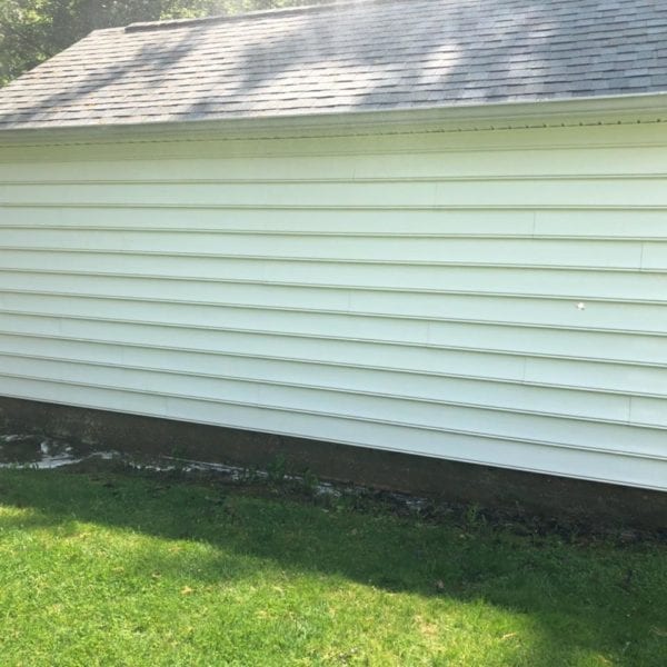 A white wooden building with a sloped roof is surrounded by lush green grass, and sunlight casts intricate shadows on its siding. This serene setting reflects the pristine results you can achieve with Maryland Pro Wash, your go-to solution for professional pressure washing services in Harford County MD, Baltimore County MD, Cecil County MD, Howard County MD, Carroll County MD, Anne Arundel County MD. Our team proudly extends its top-notch services to Wilmington DE, New Castle County DE, and Delaware County PA as well. Whether it’s enhancing the curb appeal of your home or maintaining commercial properties spotless throughout these regions, Maryland Pro Wash ensures every inch of your property shines like new—just like how sunlit shadows dance on this well-maintained building.