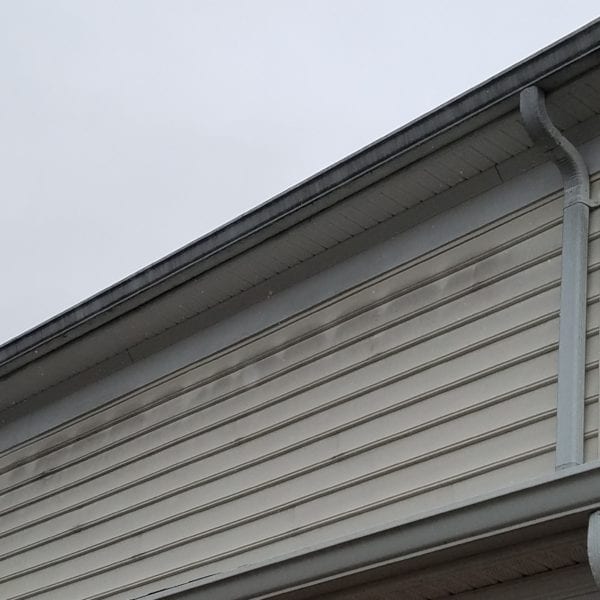 Looking at a close-up of a house exterior, we see a section featuring light-colored vinyl siding beneath the roof gutter system. The vinyl siding, while durable, appears slightly weathered with some noticeable dark streaks that detract from its otherwise pristine condition. Above it, the roof edge is neatly trimmed with a metal gutter and downspout, essential for effective water drainage.

For homeowners seeking to restore the beauty of their homes in Harford County MD, Baltimore County MD, Cecil County MD, Howard County MD, Carroll County MD, Anne Arundel County MD as well as Wilmington DE and New Castle County DE in Delaware or Delaware County PA in Pennsylvania – Maryland Pro Wash offers professional pressure washing services tailored to eliminate these kinds of imperfections. Specializing in cleaning and revitalizing surfaces like yours with care and precision ensures your home stands out for all the right reasons.
