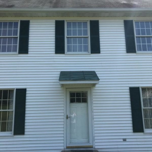 Imagine a charming white two-story house with dark shutters elegantly framing each window. The front entrance features a small overhang, providing a welcoming touch, flanked by two sets of double windows that allow natural light to spill into the home. While picturesque, the roof shows gentle signs of weathering, hinting at years of weather exposure.

For homeowners in areas such as Harford County MD, Baltimore County MD, Cecil County MD, Howard County MD, Carroll County MD, Anne Arundel County MD; Wilmington DE; New Castle County DE; and Delaware County PA who seek to restore their homes' pristine appearance while preserving structural integrity against such elements — Maryland Pro Wash stands as an expert solution. Offering professional pressure washing services tailored for this stunning architectural style and more. Maryland Pro Wash ensures every surface gleams like new again while taking care not to disturb charming features unique to properties across these regions.