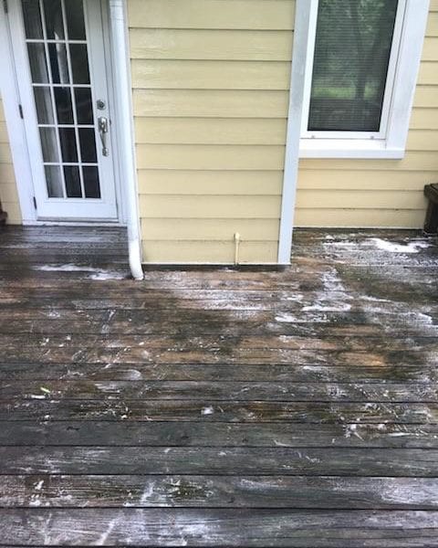 A wooden deck with weathered planks, showing clear signs of recent cleaning activity, sits next to a charming yellow house with pristine white trim. The partial wetness of the wood highlights the effectiveness of the cleaning process. On the house wall, a sparkling glass-paneled door and a gleaming window reflect the thorough maintenance undertaken. This scene perfectly captures what Maryland Pro Wash specializes in—providing top-notch pressure washing services to revitalize outdoor spaces in Harford County MD, Baltimore County MD, Cecil County MD, Howard County MD, Carroll County MD, Anne Arundel County MD. Their expertise extends beyond Maryland as they serve Wilmington DE and New Castle County DE effectively and professionally. Additionally, they offer their exceptional services across Delaware County PA ensuring every deck becomes as immaculate as this one beside its sunlit abode.